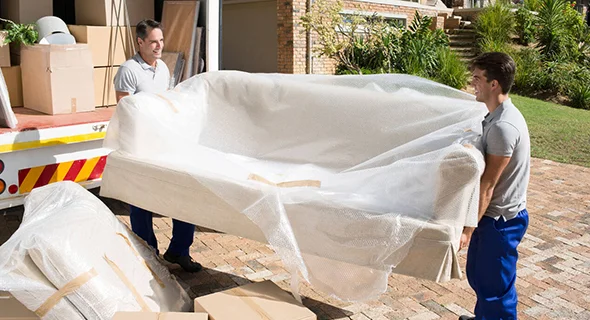 Movers carefully transporting a couch for urgent goods relocation in La Porte, IN.